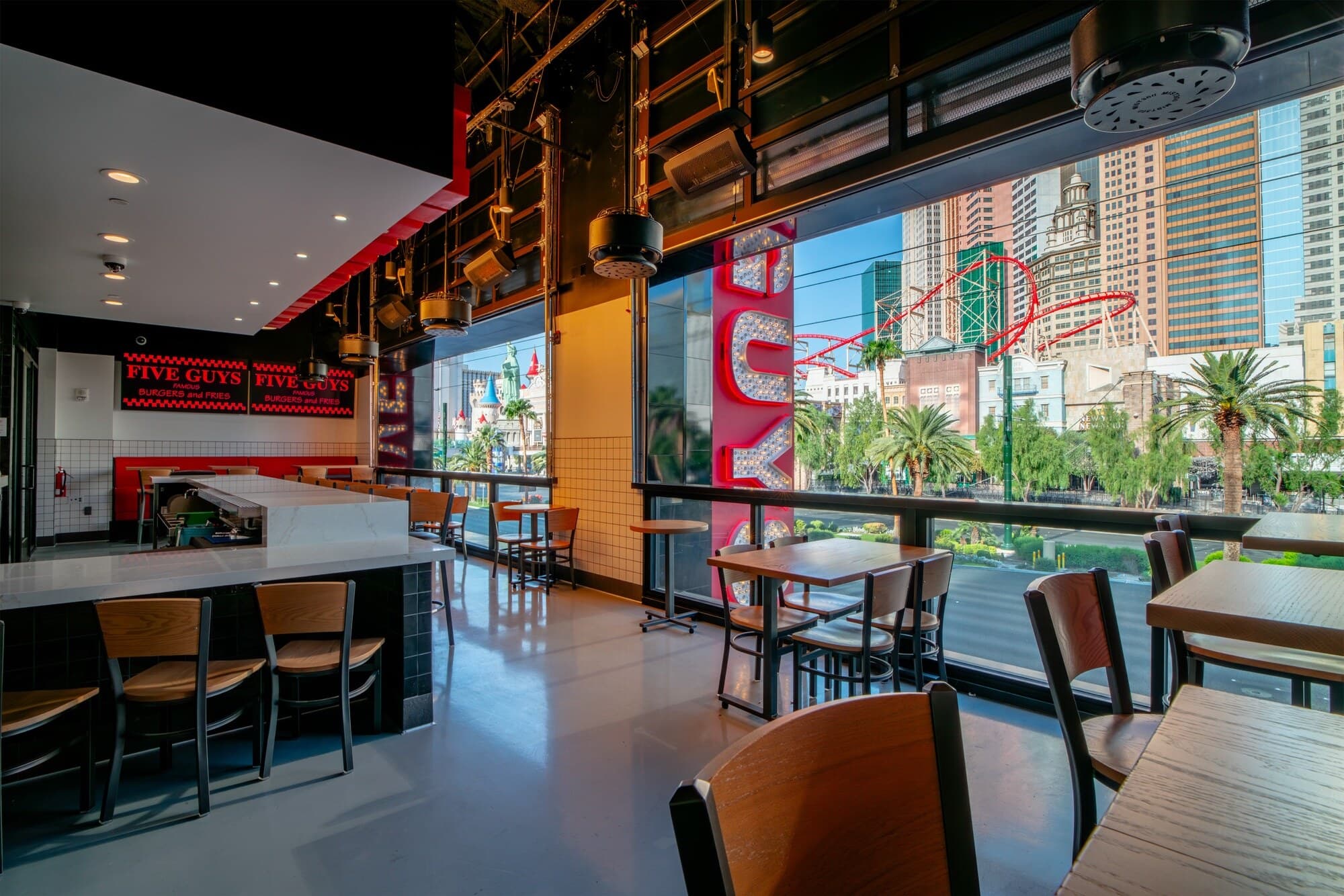 Five Guys Showcase dining room with floor-to-ceiling open window walls overlooking the Las Vegas Strip, New York-New York's skyline and roller coaster visible across the street