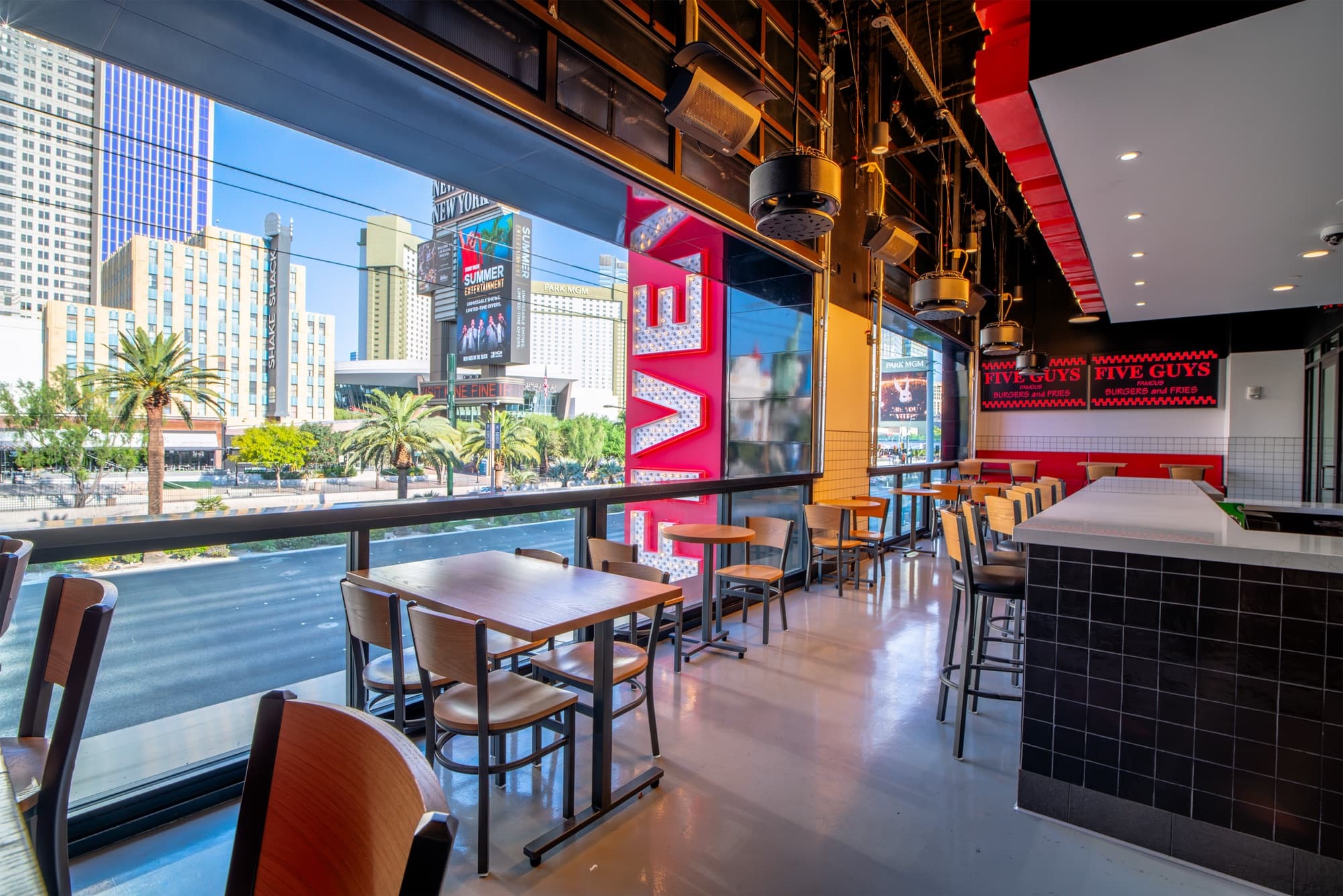 Window-rail seating along the glass at Five Guys Showcase with giant FIVE marquee letters and views of New York-New York and Park MGM