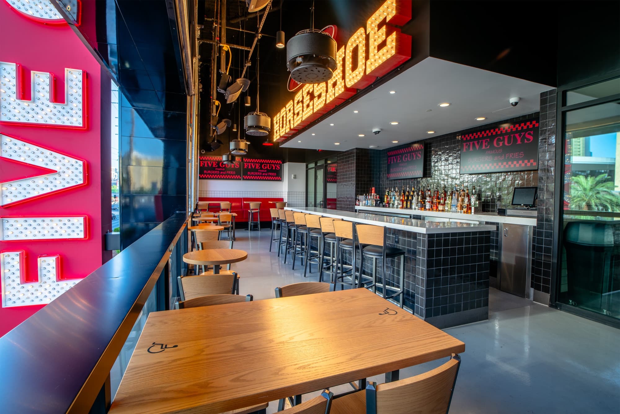 Upstairs bar at Five Guys Showcase with a vintage HORSESHOE bulb-marquee sign above the liquor display and roughly ten bar stools