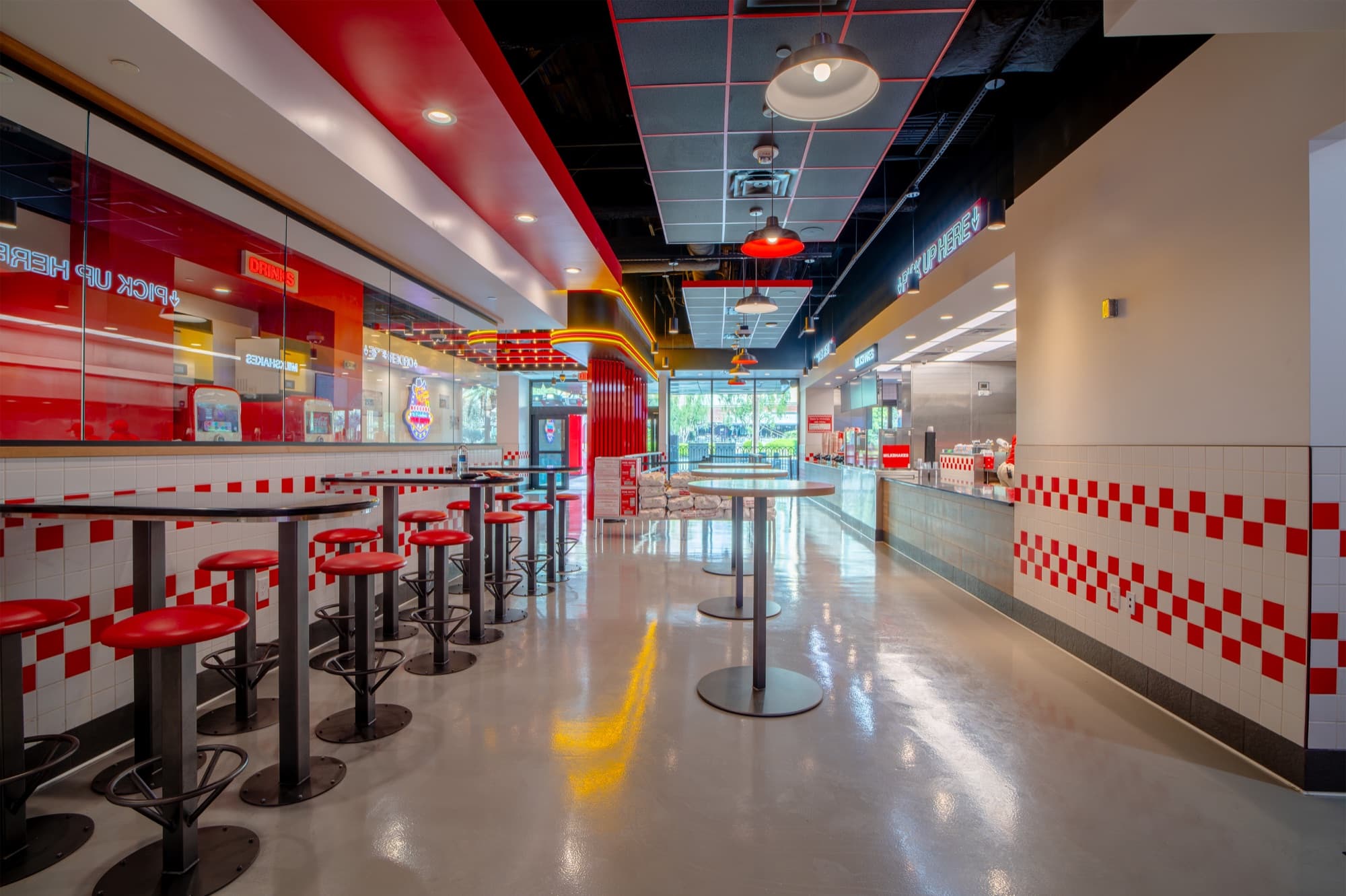 Ground-floor order counter at Five Guys Showcase with classic red-and-white checker tile, neon PICK UP HERE sign, and milkshake stations