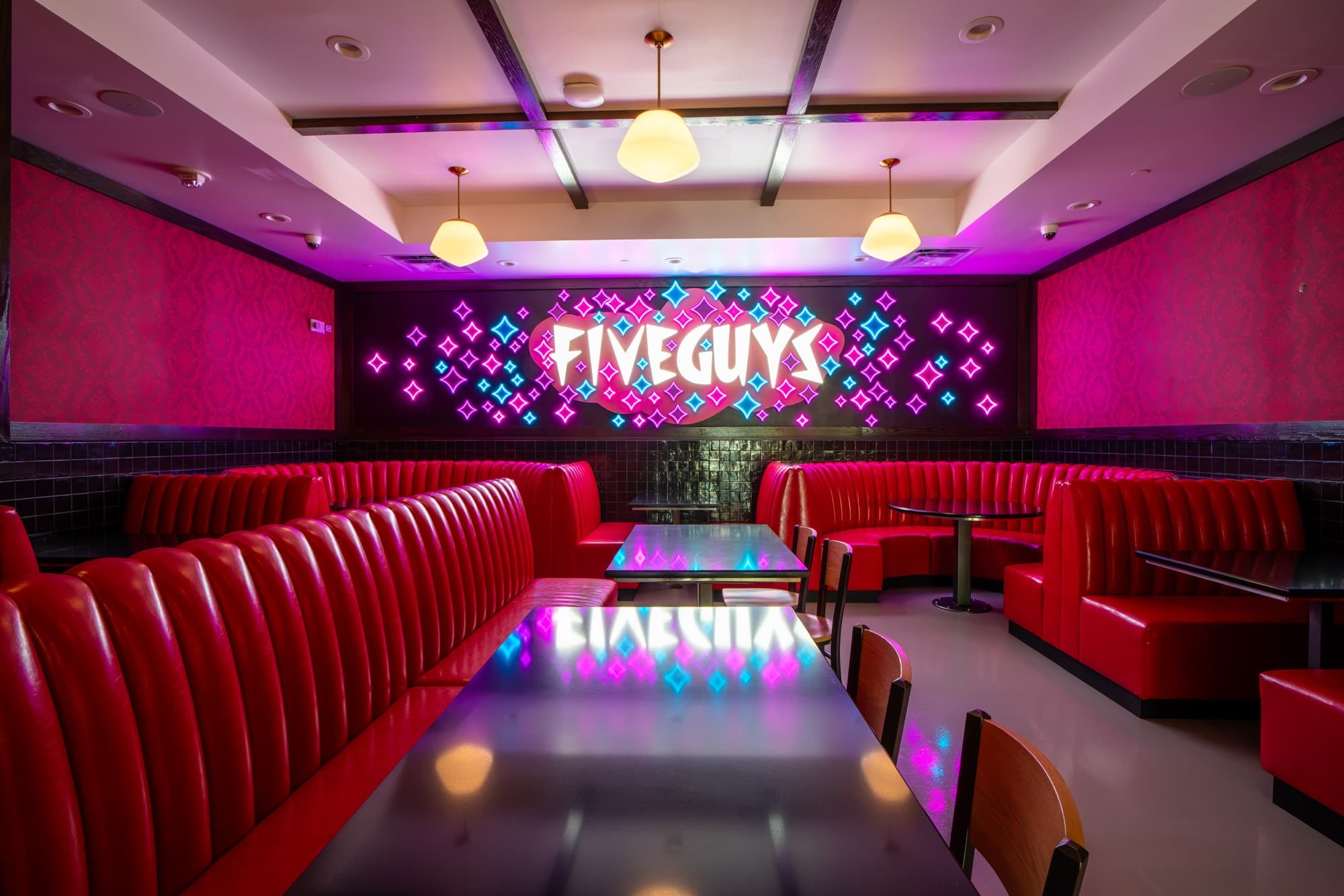 Private event lounge at Five Guys Showcase: red channel-tufted booths, black tables, and wall-length neon Five Guys signage in a casino sparkle motif