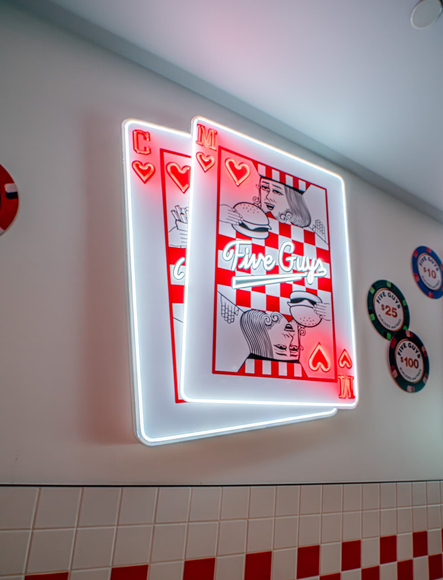 Neon wall art at Five Guys Showcase of two overlapping playing cards whose face cards hold a burger and a milkshake, surrounded by Five Guys poker chips
