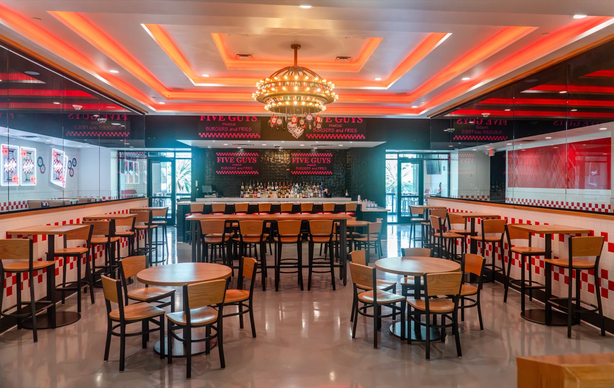 Main upstairs dining room at Five Guys Showcase with a roulette-wheel chandelier centerpiece, red cove-lit ceiling, and mixed table seating