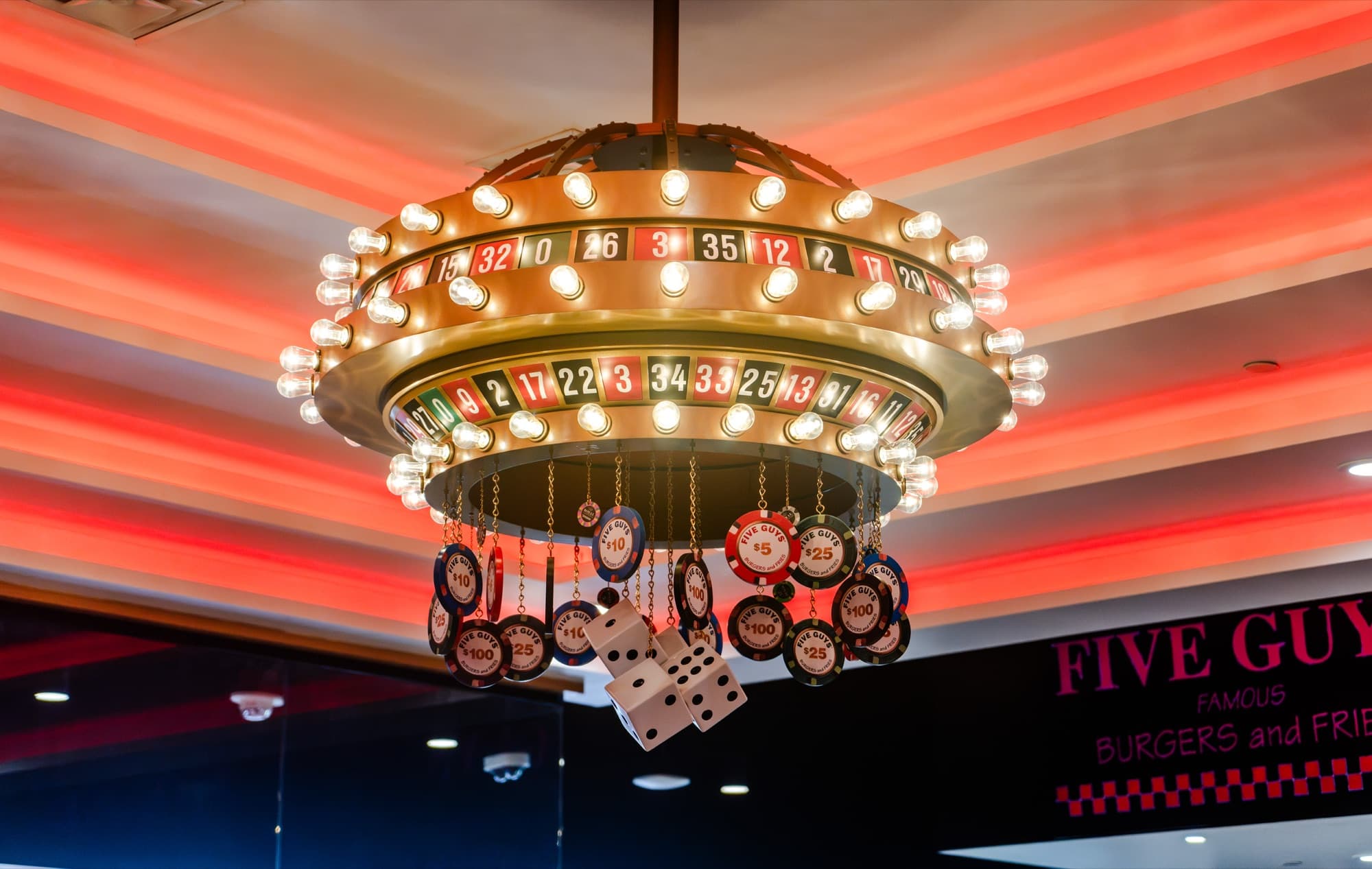 Detail of the roulette-wheel chandelier at Five Guys Showcase, ringed with marquee bulbs and hung with Five Guys-branded poker chips and giant dice